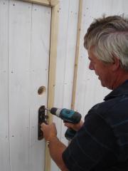 Pete fixes the old latch in place on the new door.